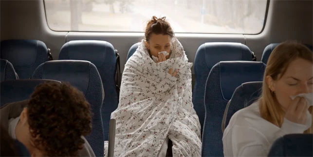 Förkyld kvinna invirad i täcke på bussen på väg till jobbet.